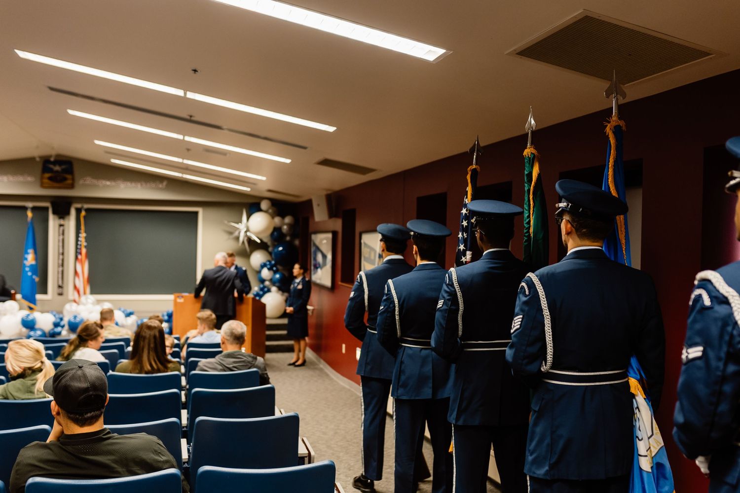 Military personnel stand at attention during formal ceremony in conference room.