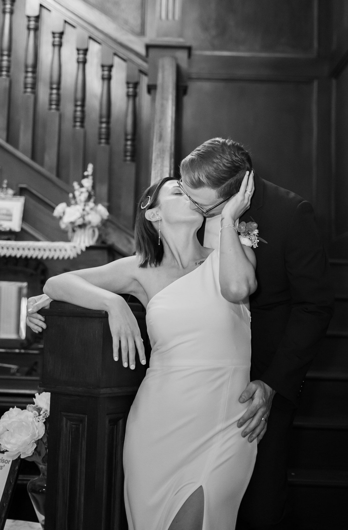 Black and white photo of a couple sharing a kiss in an elegant staircase setting.