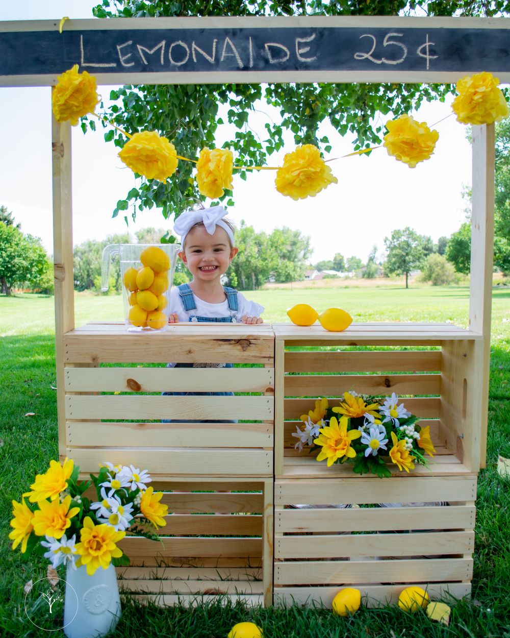 Rustic wooden lemonade stand decorated with yellow flowers and lemons in outdoor setting.
