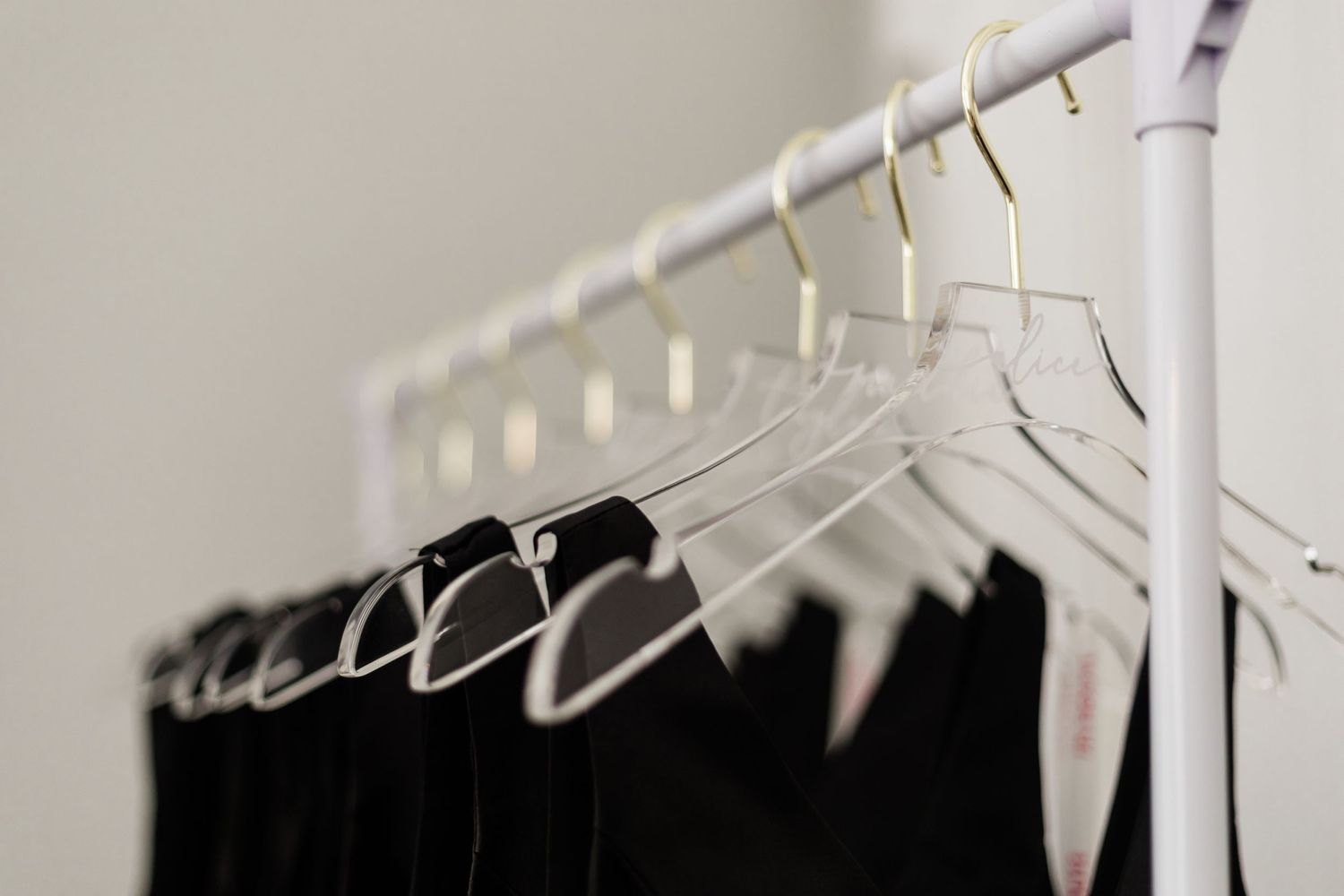 Minimal composition of black dresses hanging on white hangers against a light wall.