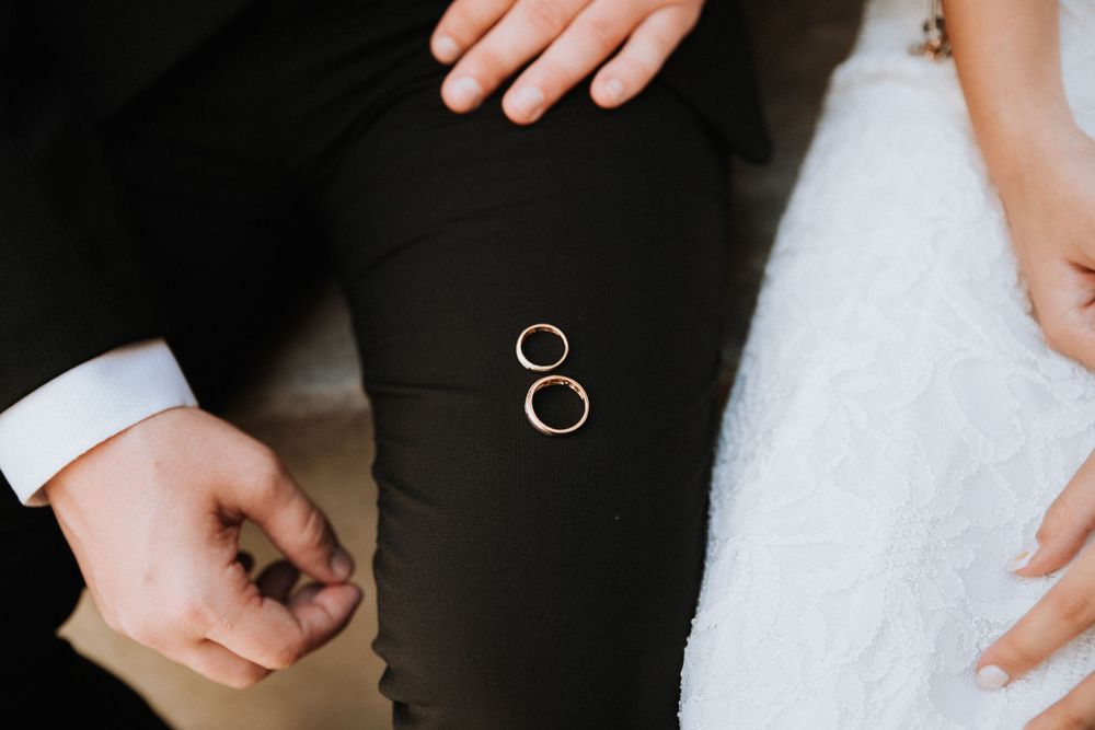 Closeup of wedding rings resting on the groom’s pantsuit, sitting beside the bride, preparing for the exchange of rings.