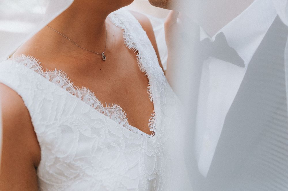 Closeup under the bride’s veil, with the bride and groom’s bodies close together on their wedding day.