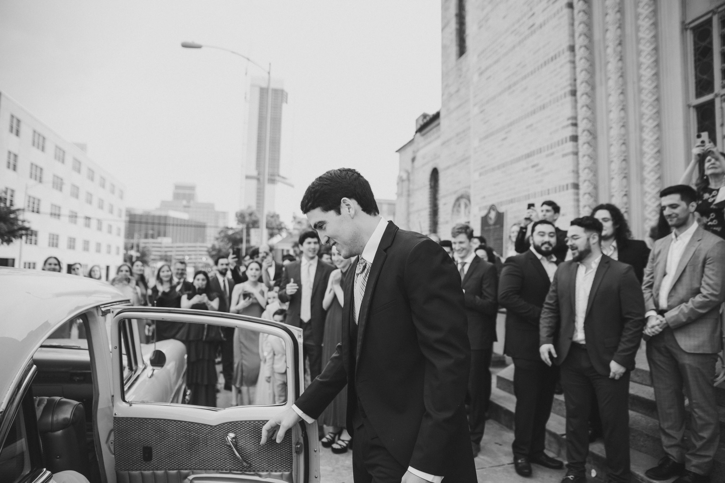Groom opening the car door of his getaway car after the wedding ceremony, capturing a tender moment as he leads his bride away.