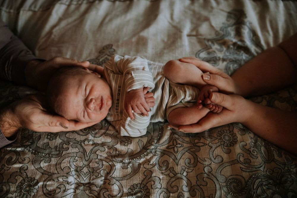 Newborn baby peacefully cradled in the hands of both parents, with their hands gently cupping the baby’s head and feet, symbolizing love.