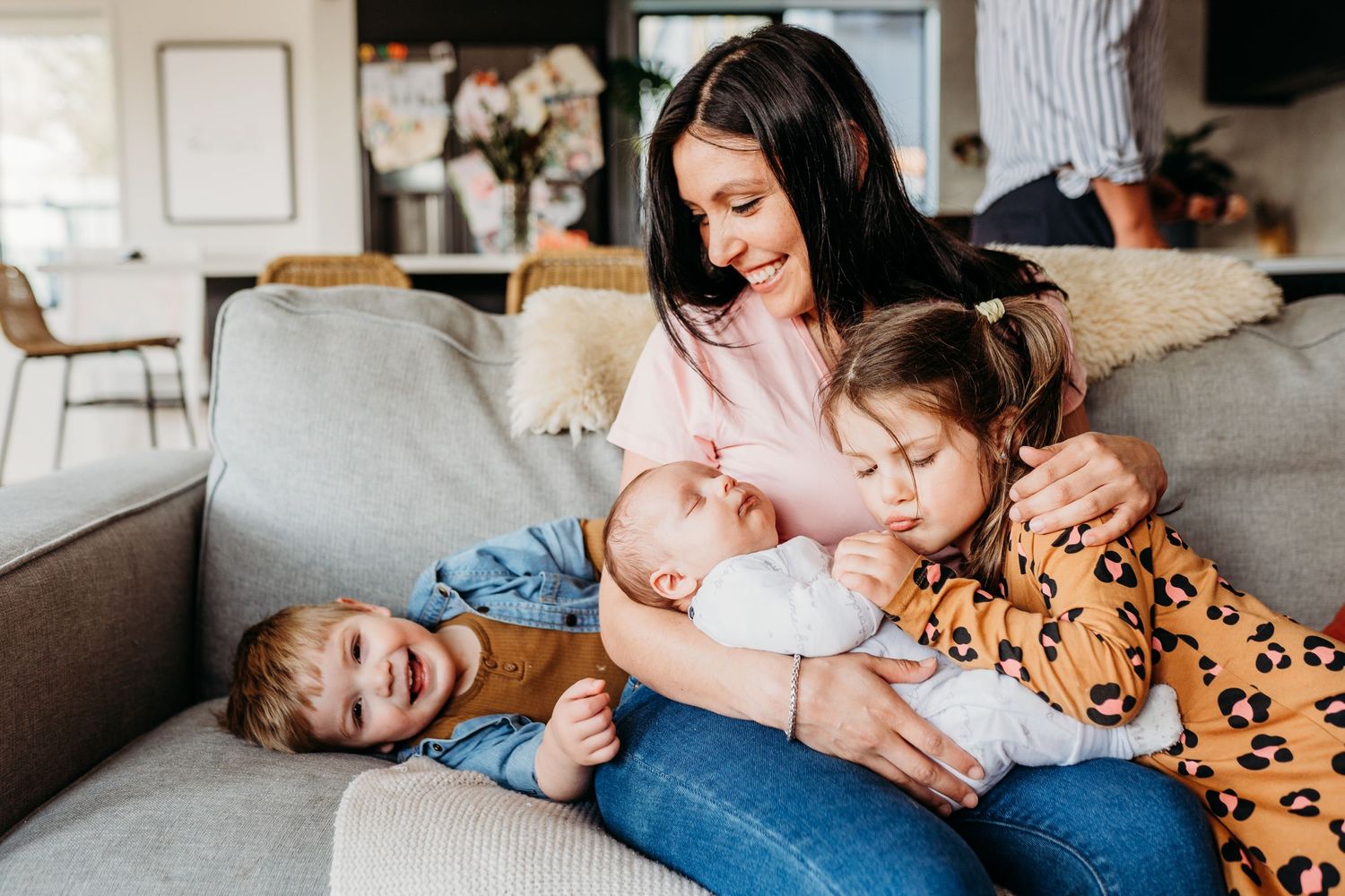 A heartwarming family scene on a grey couch with three children sharing cuddles.