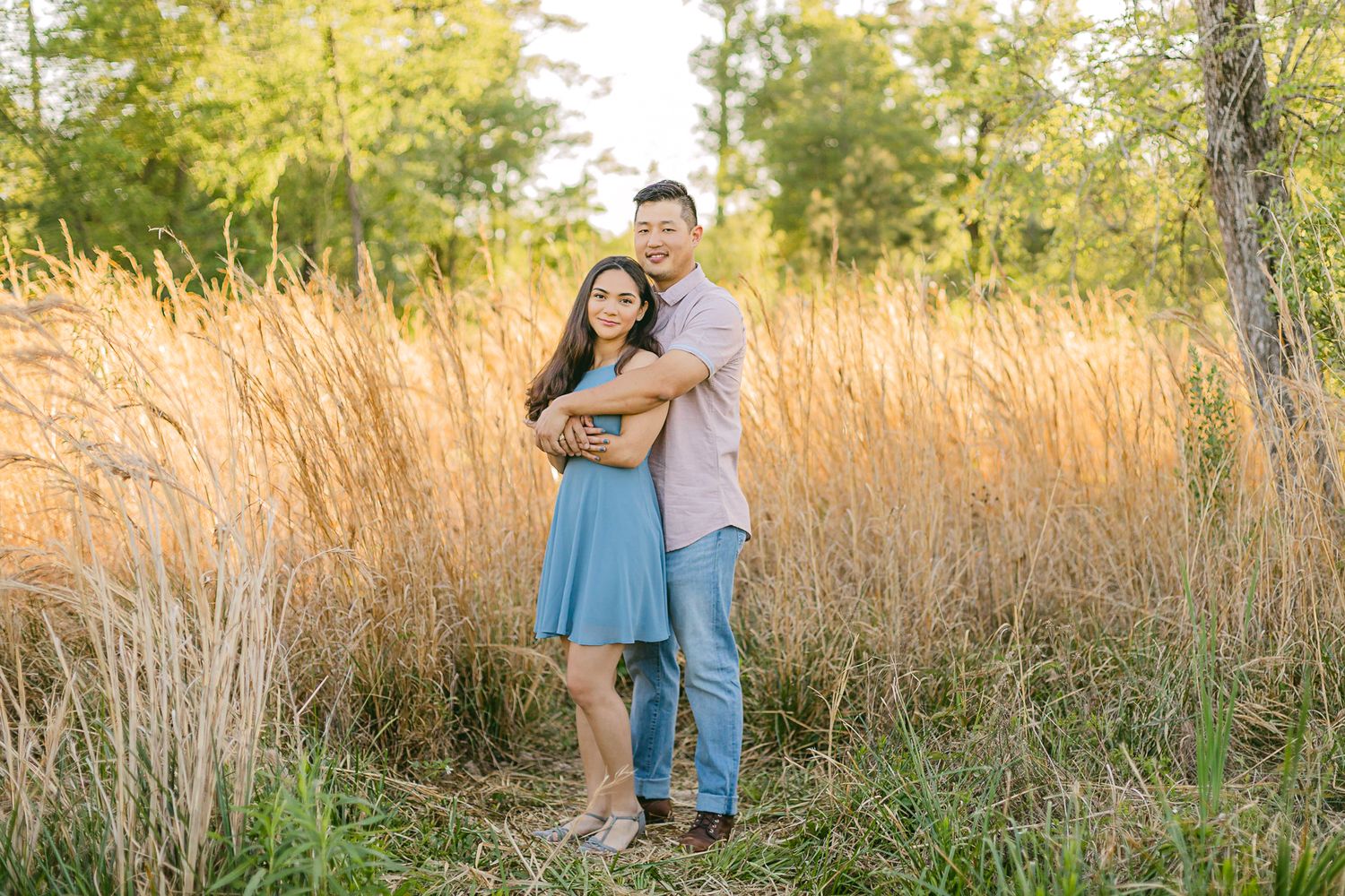 A couple embraces in a field of tall grass in the evening light.