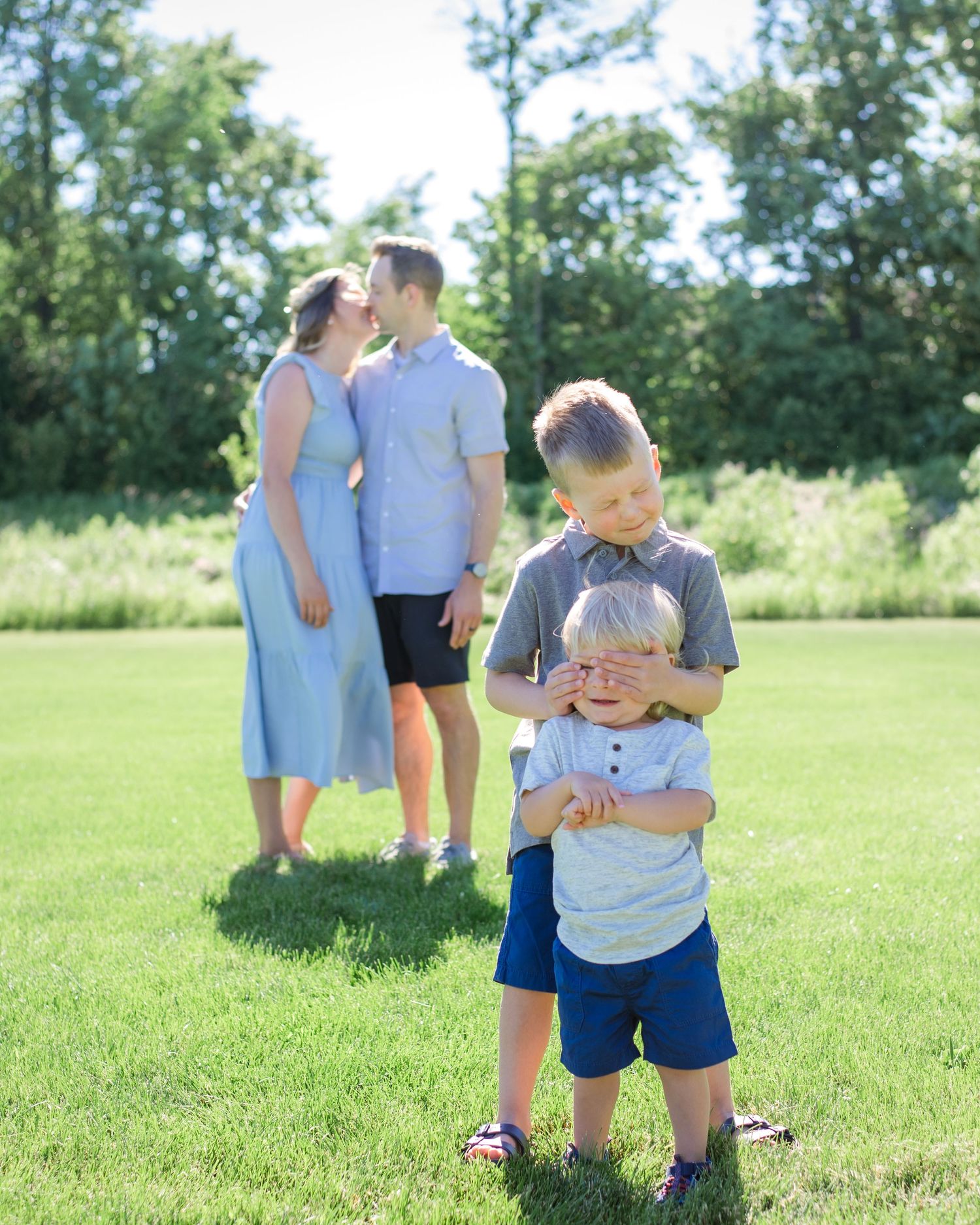 A sweet family moment captured in a grassy field with kids playing in the foreground.
