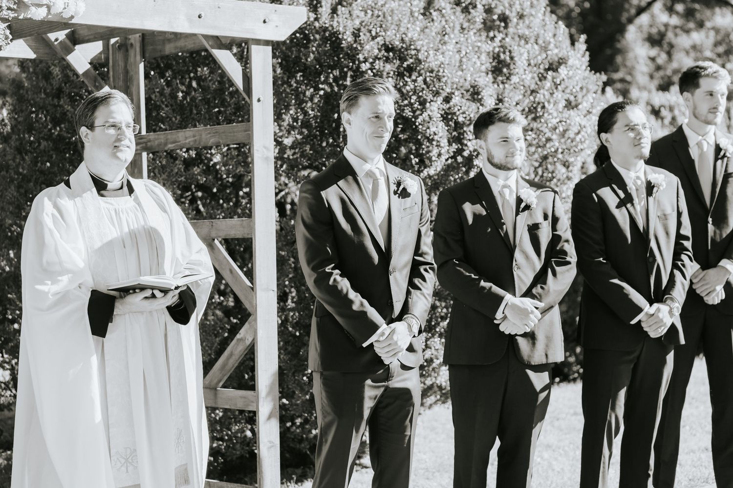 Black and white photo of wedding ceremony with officiant and groomsmen at outdoor altar.