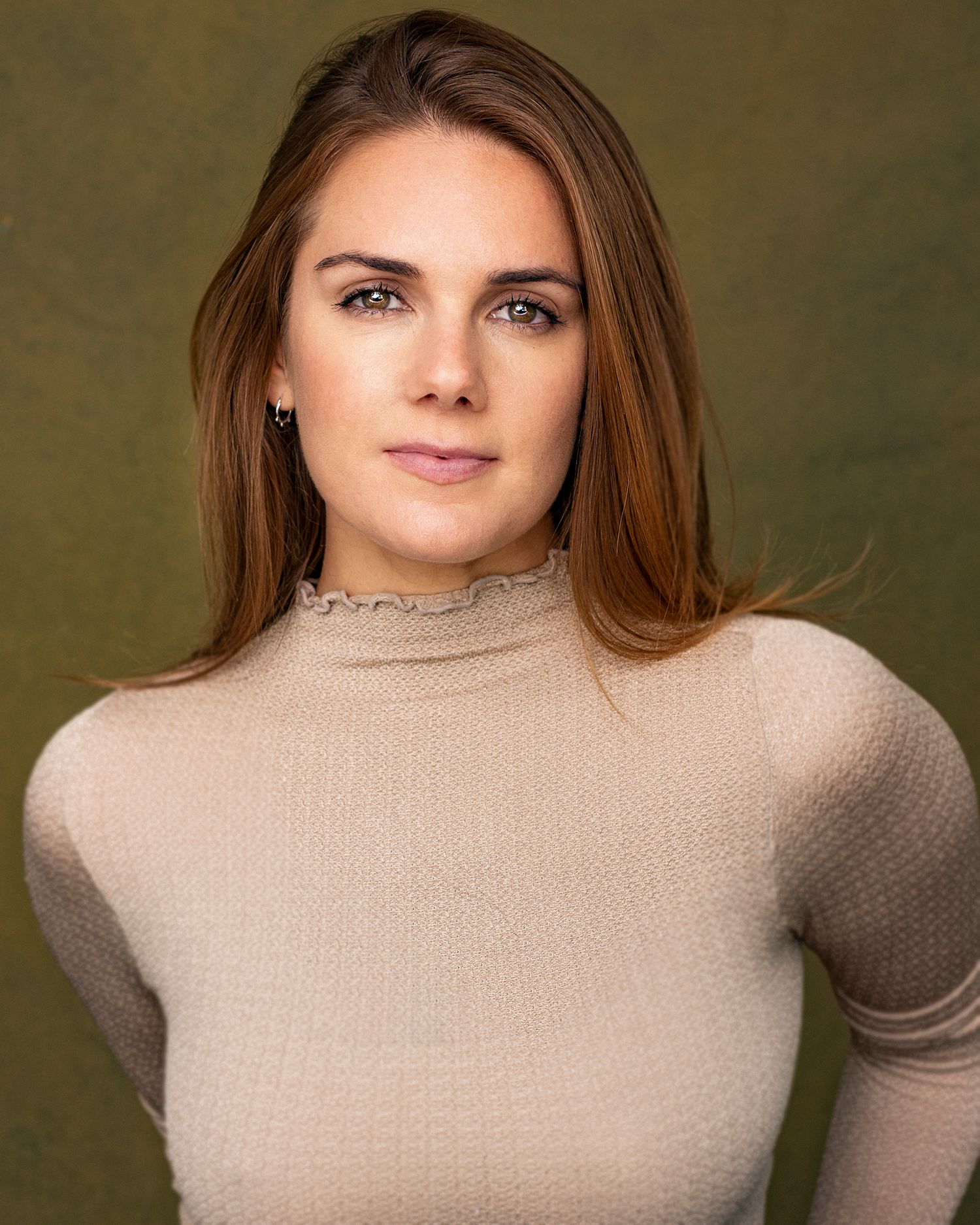 Professional headshot with long brown hair wearing beige turtleneck sweater against olive backdrop.