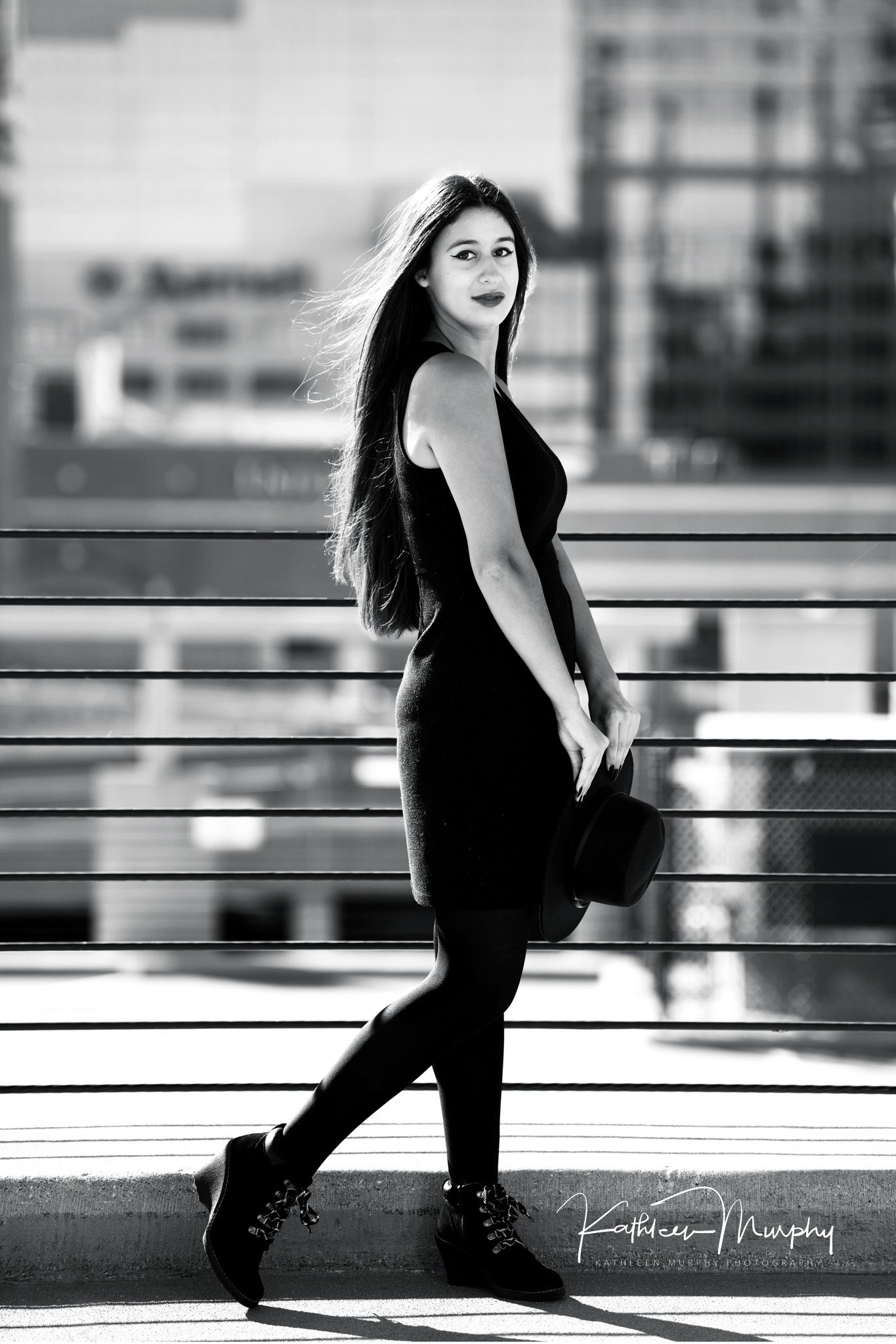Black and white urban fashion portrait on a modern balcony with cityscape backdrop.