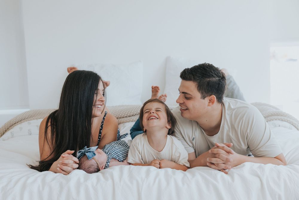 A family laughs together in a lifestyle in-home newborn photoshoot near American Fork, Utah with a local photographer.