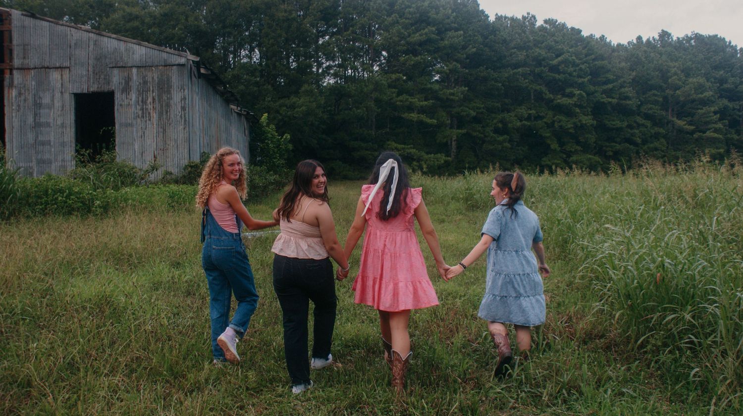 Group walking together through tall grass field near concrete structure on summer day.