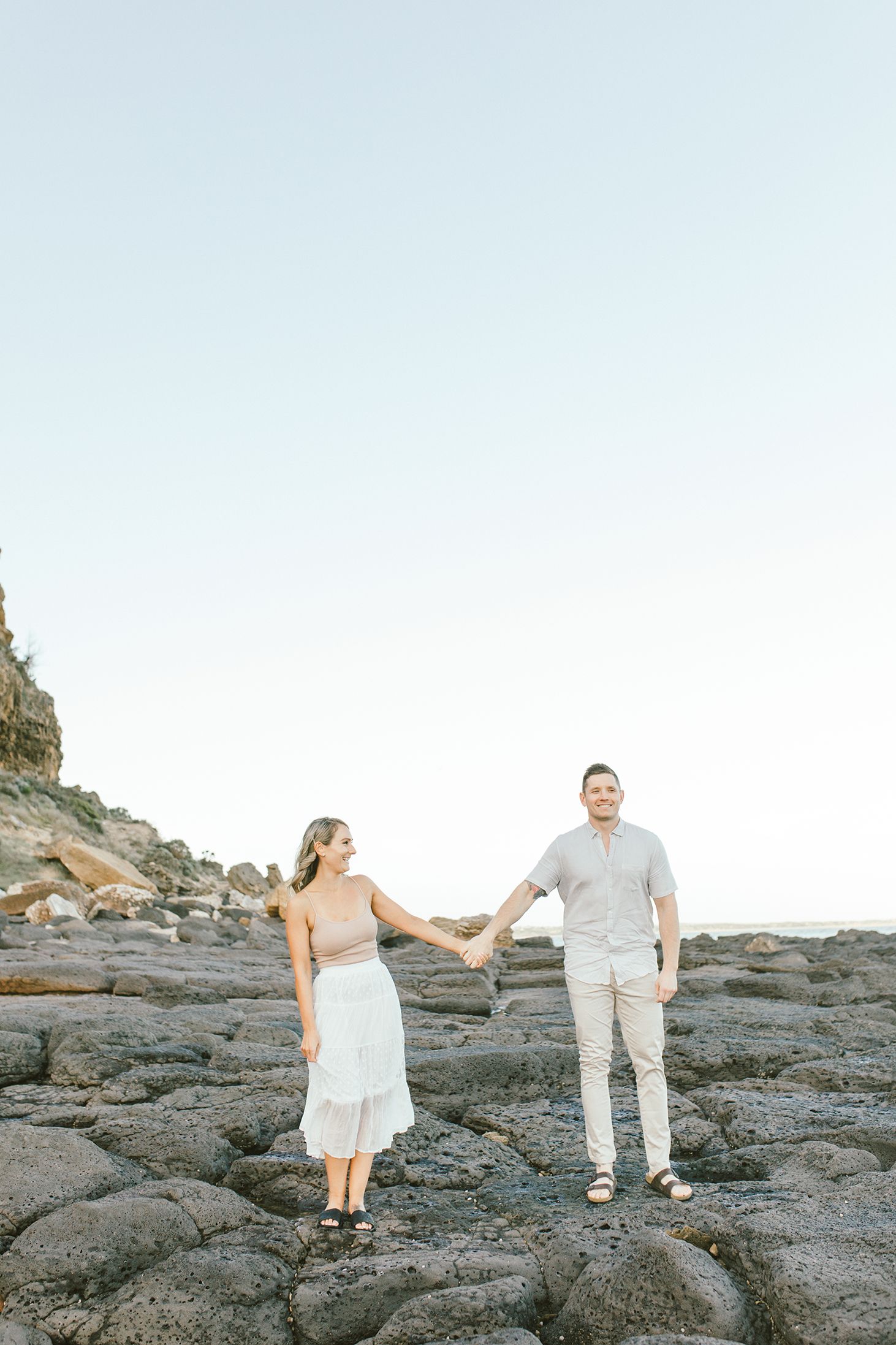 Two people standing on rocky coastal formations with cliffs in the background.