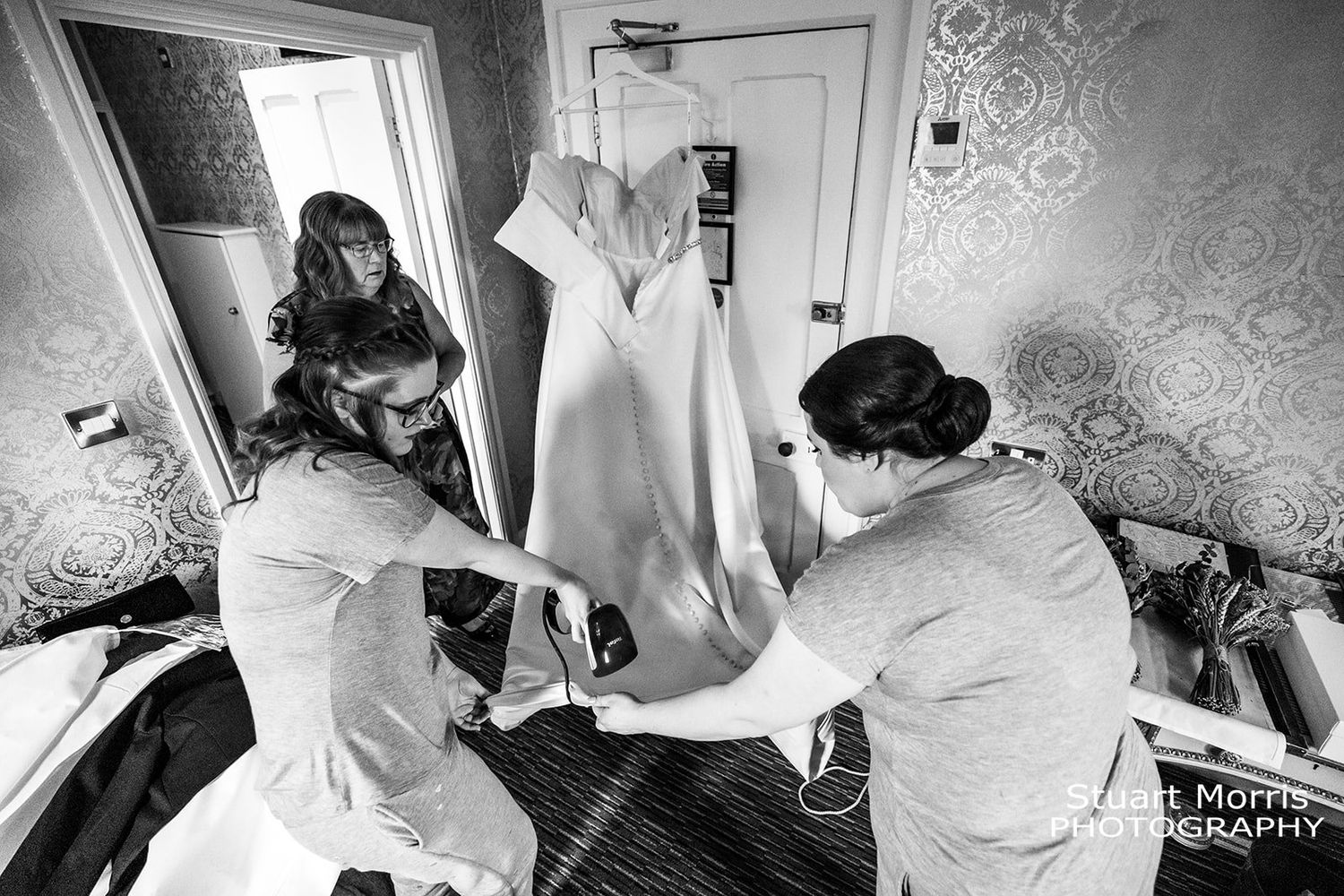 bride and bridesmaid steam the wedding dress during the bridal prep at Ruthin castle. Stuart Morris Photography.