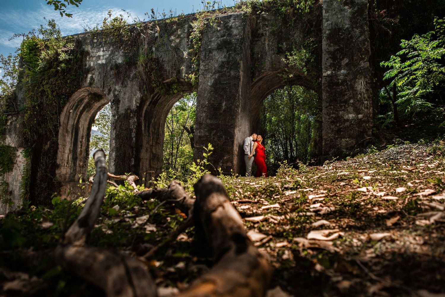 Stone archway ruins with vegetation growing on top in a scenic outdoor setting.