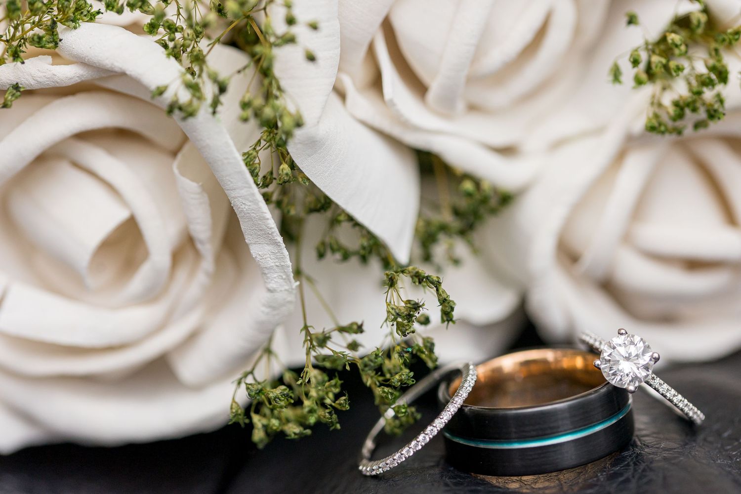 Close-up of wedding rings and white roses with green accents on dark background in elegant macro shot.