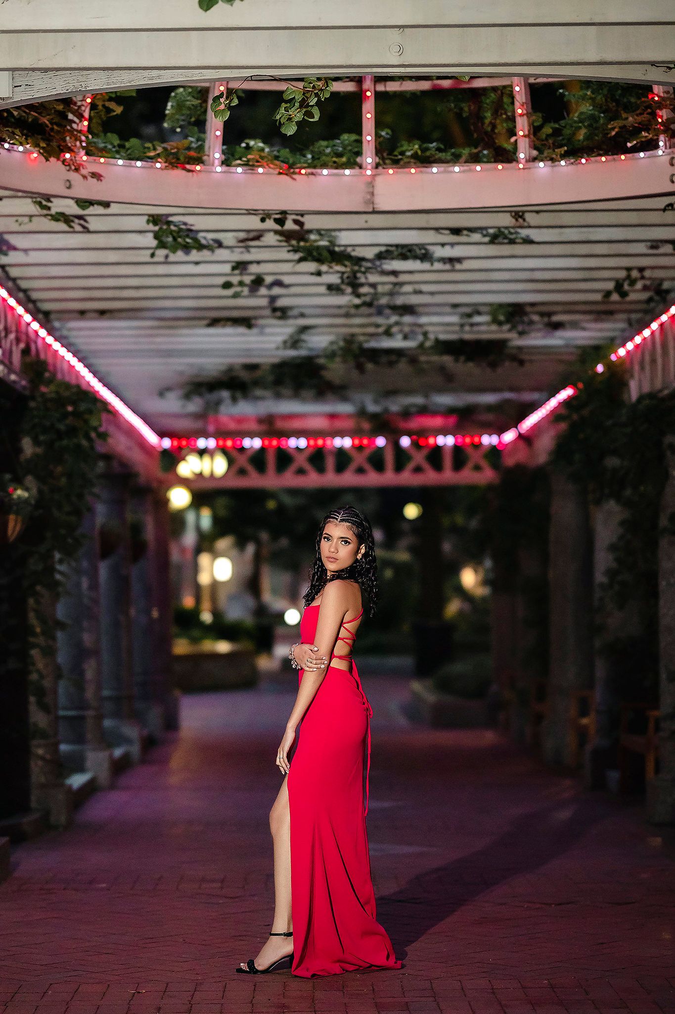 Evening portrait session under pink-lit pergola featuring elegant red formal dress.
