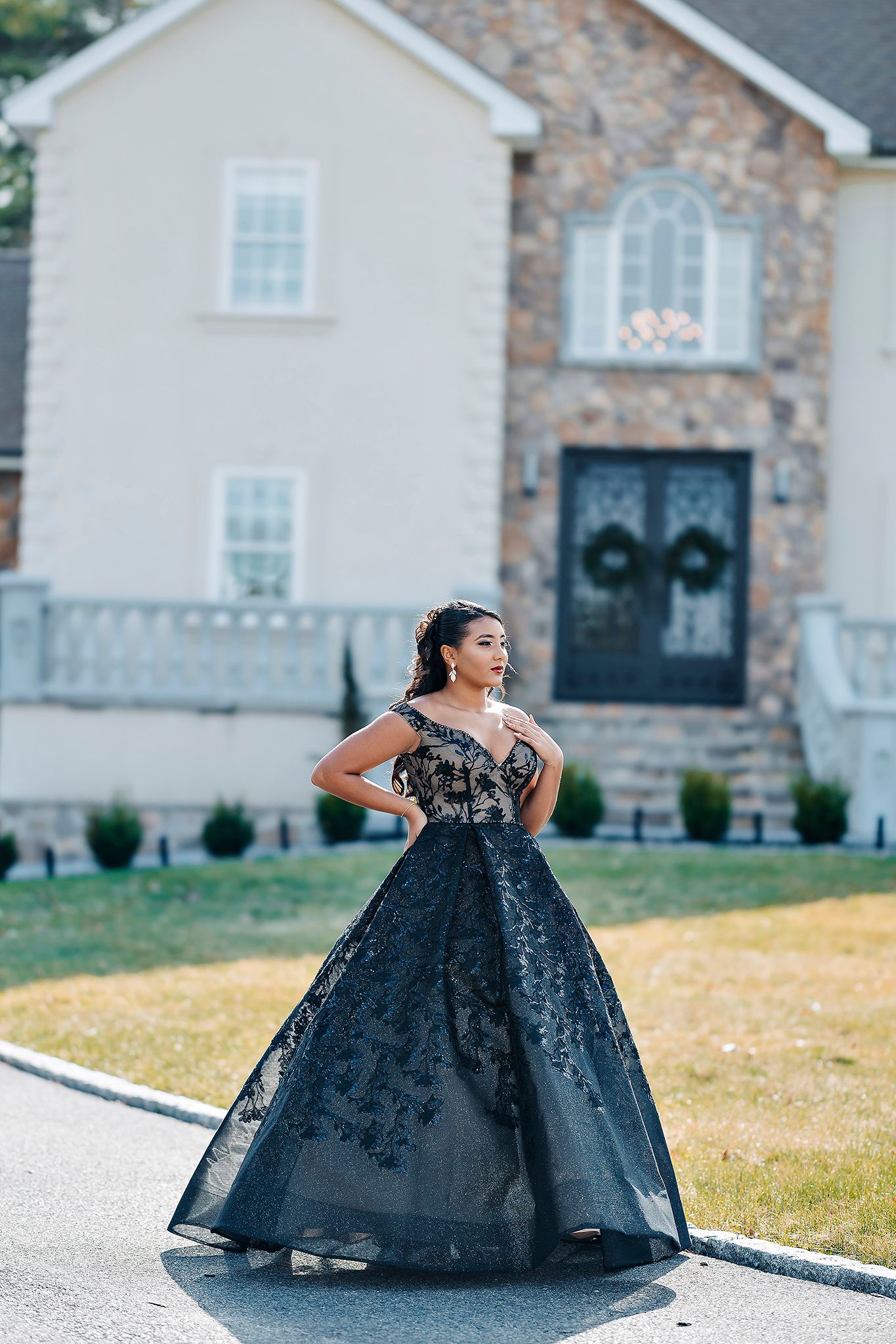 Glamorous black ball gown photographed in front of a stone and stucco luxury home with decorative wreaths.