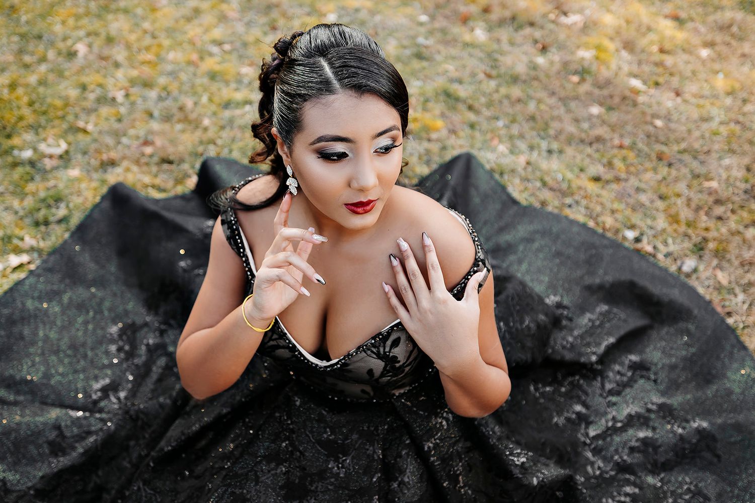 Dramatic high-angle portrait showcasing intricate details of a black formal gown against autumn ground.