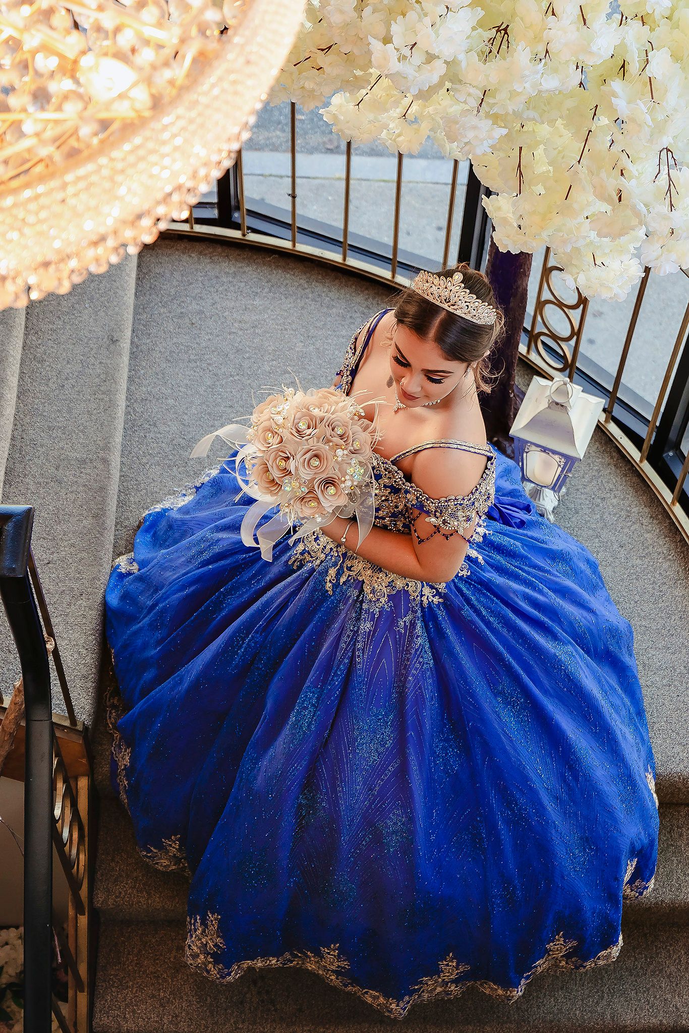 Ornate royal blue ball gown with crystal details spread out on grey steps.