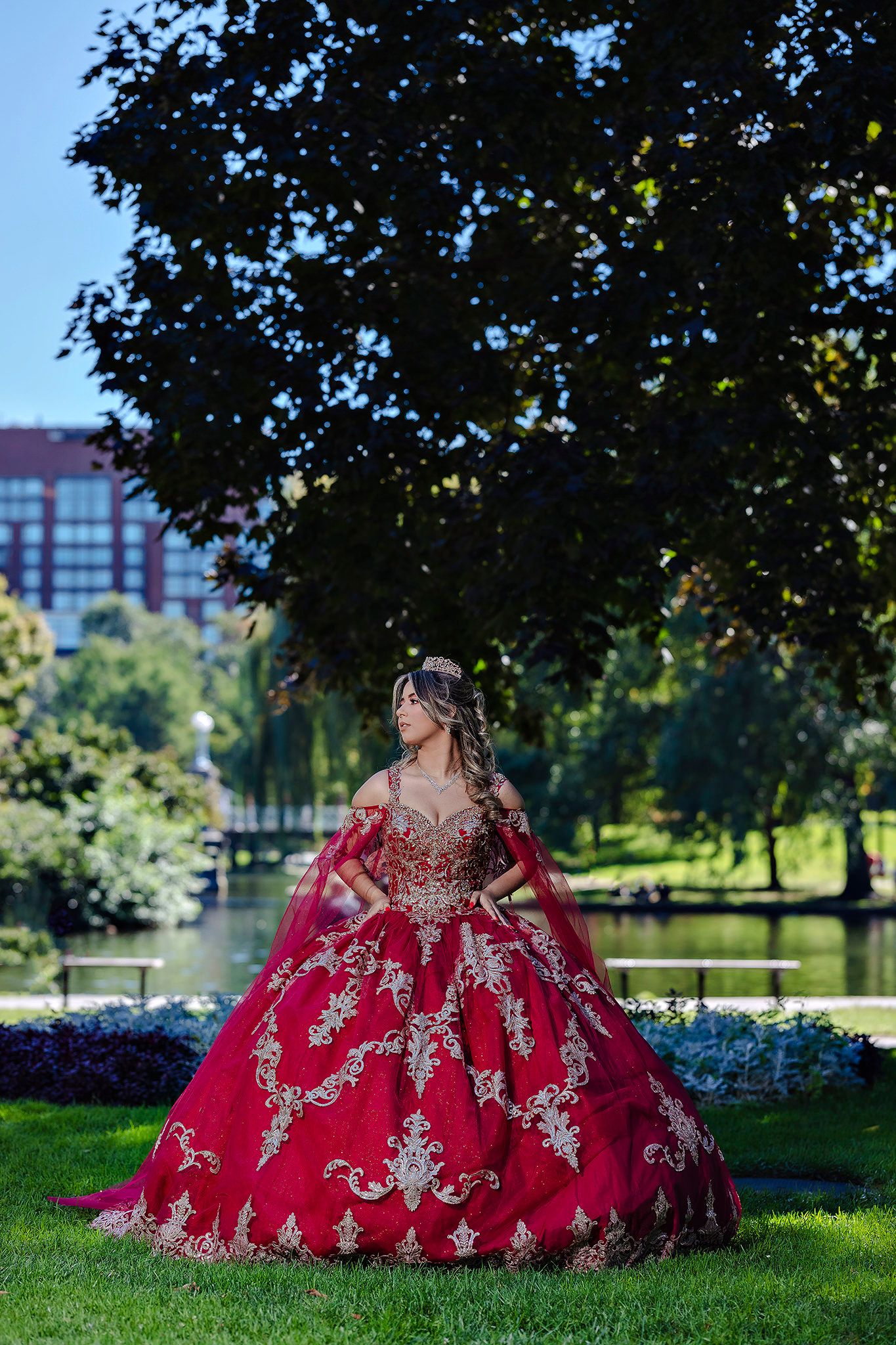 Stunning red and gold embroidered ball gown photographed in a sunny park setting.