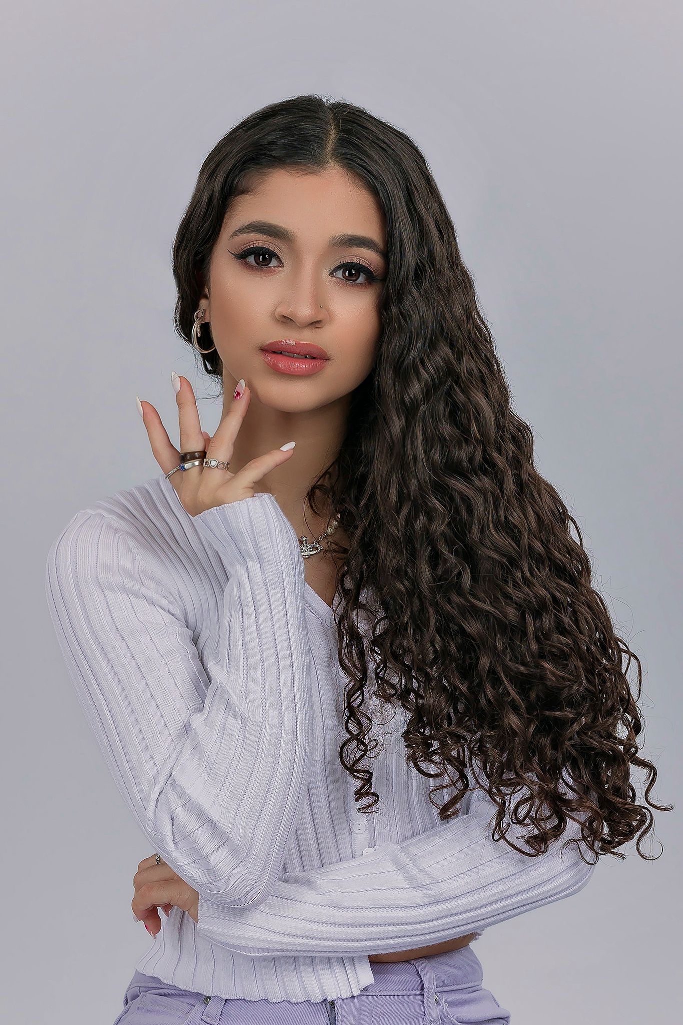 Model in white ribbed sweater showing different poses against gray backdrop with curly dark hair styled naturally.