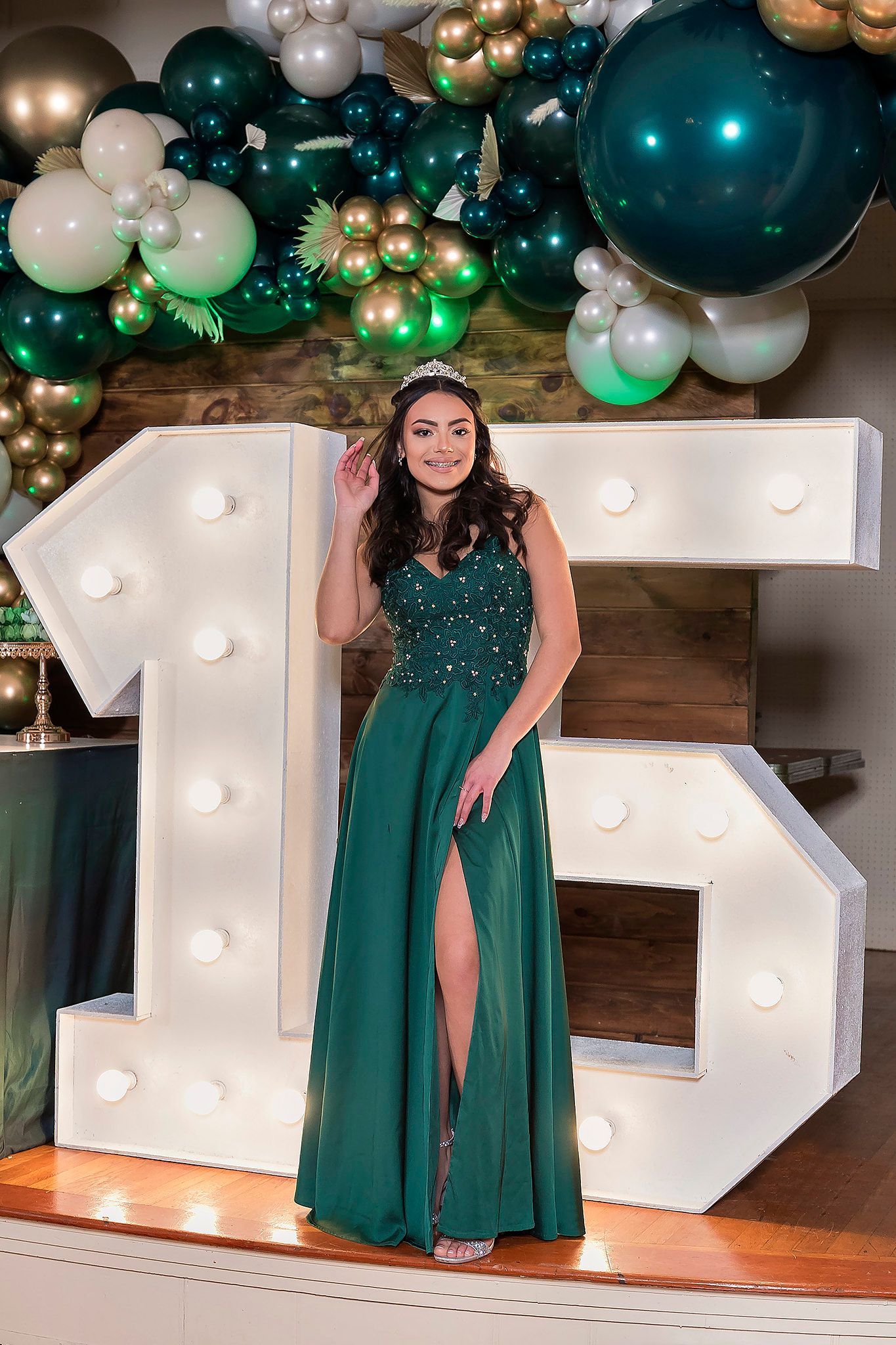Green balloon arch and illuminated marquee numbers create an elegant party backdrop with emerald colored evening dress.
