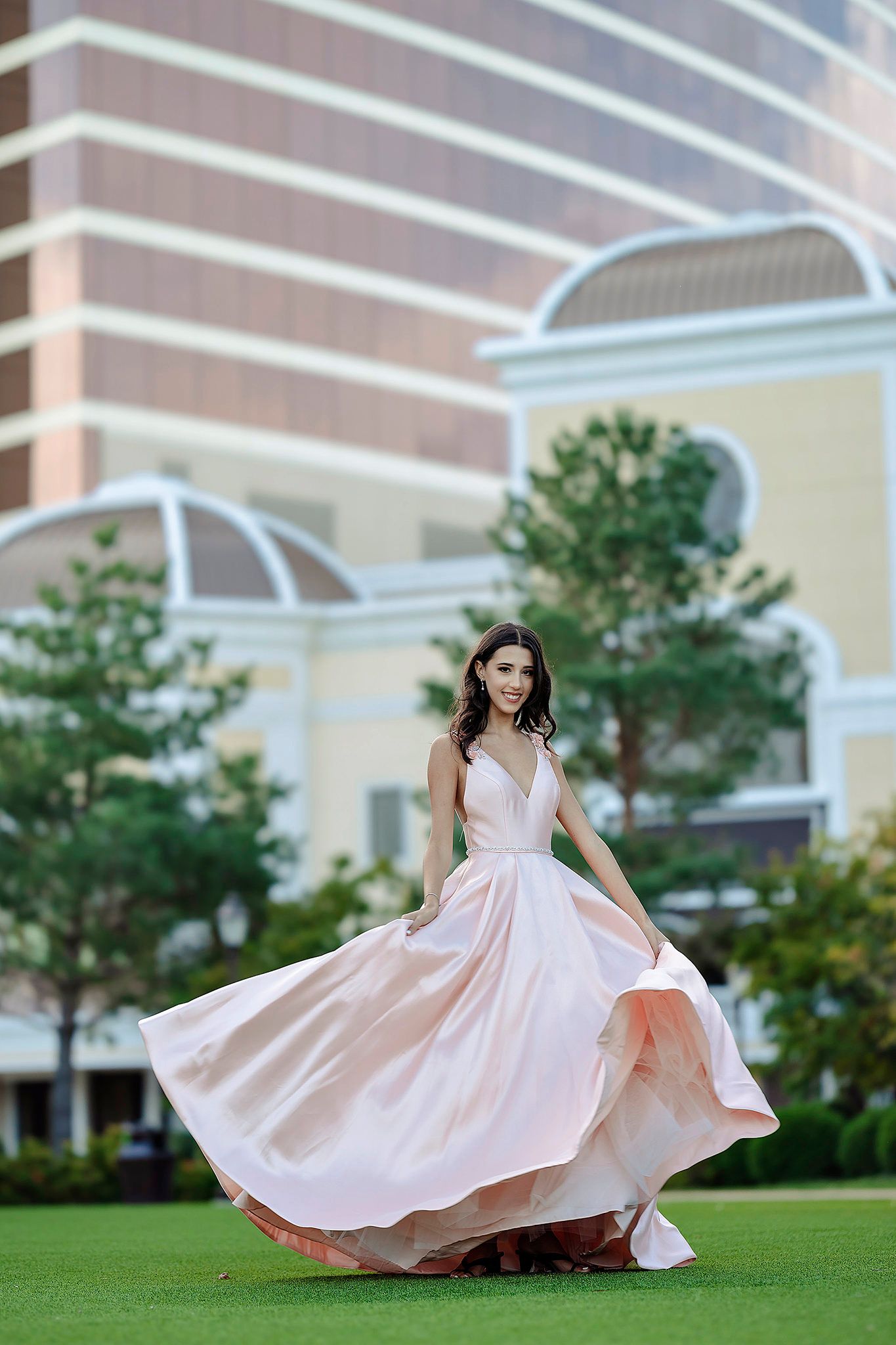 Pink ballgown dress twirls elegantly on manicured lawn with building backdrop.