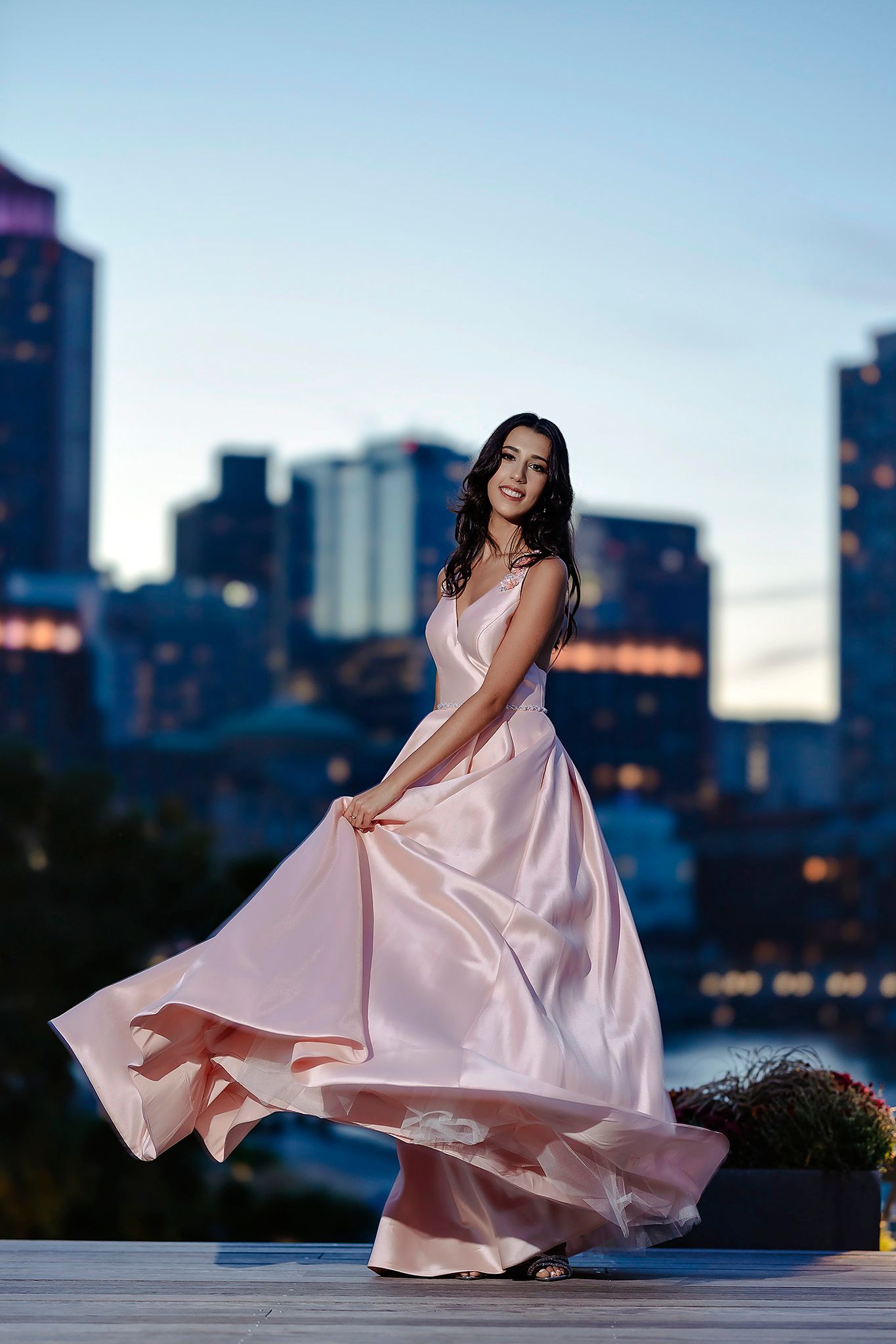 Flowing pink evening gown swirls dramatically against city skyline at dusk.