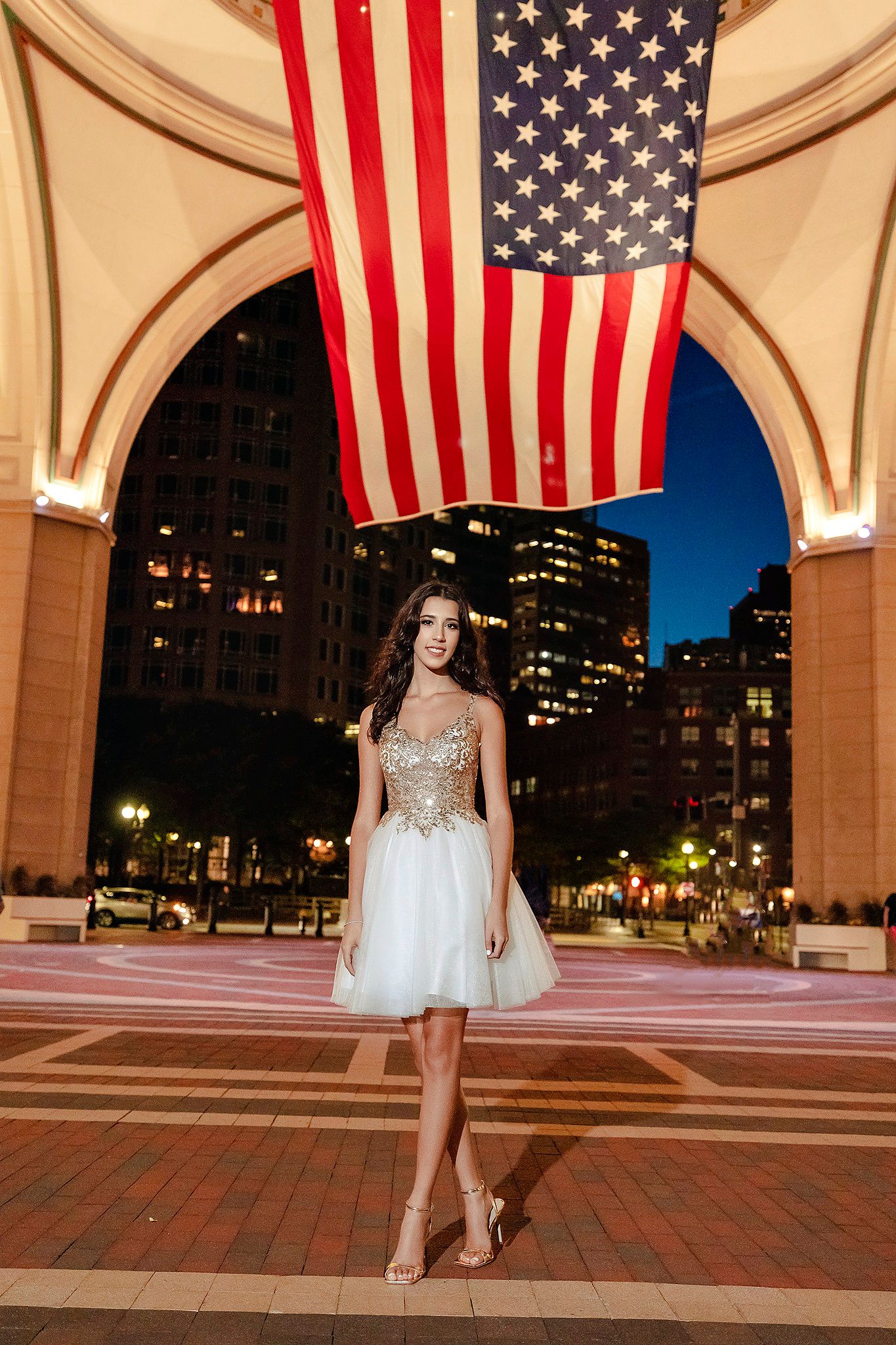 Elegant white cocktail dress under American flag in urban archway at night.