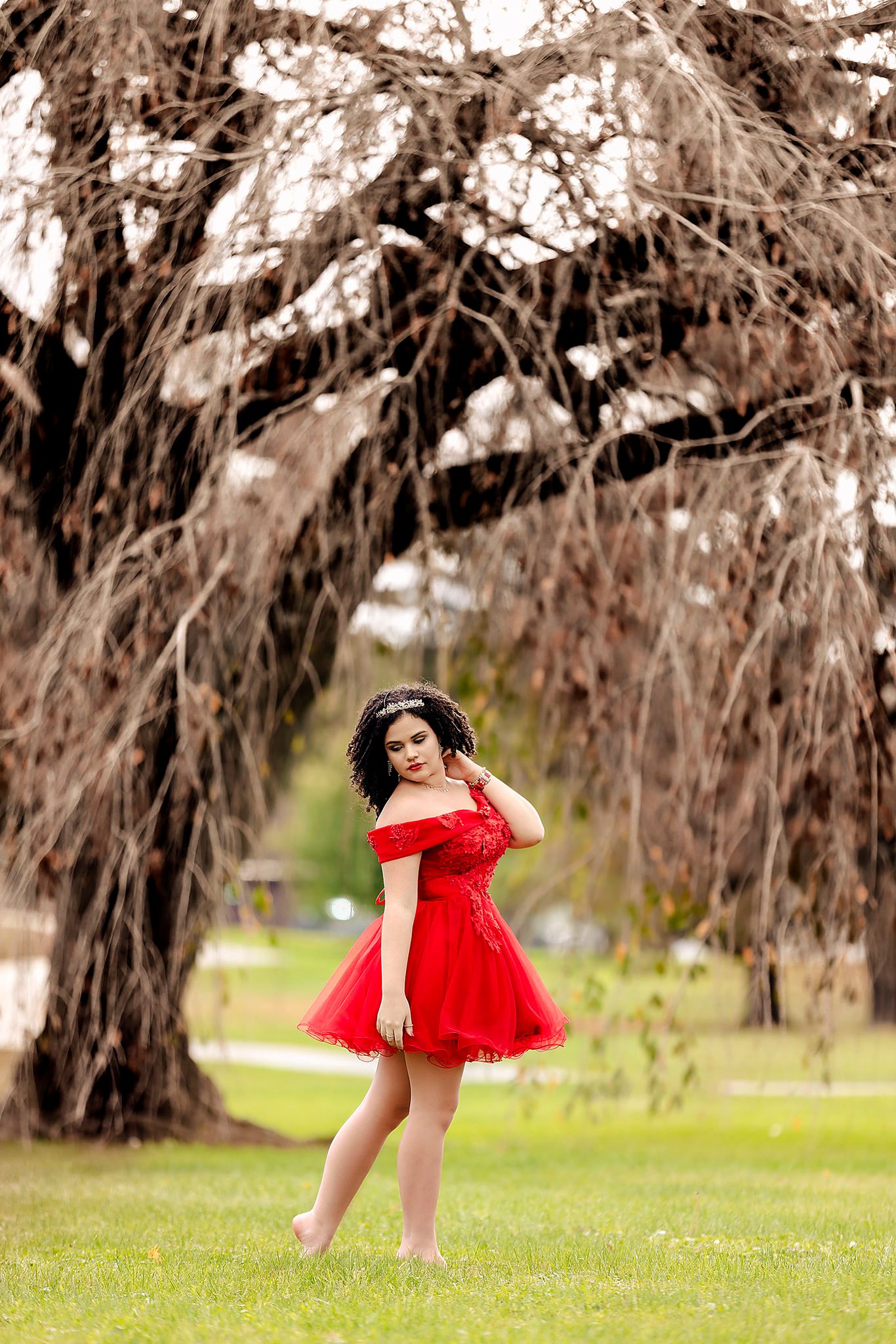 Red tulle dress twirls beneath overhanging trees in dreamy outdoor setting.
