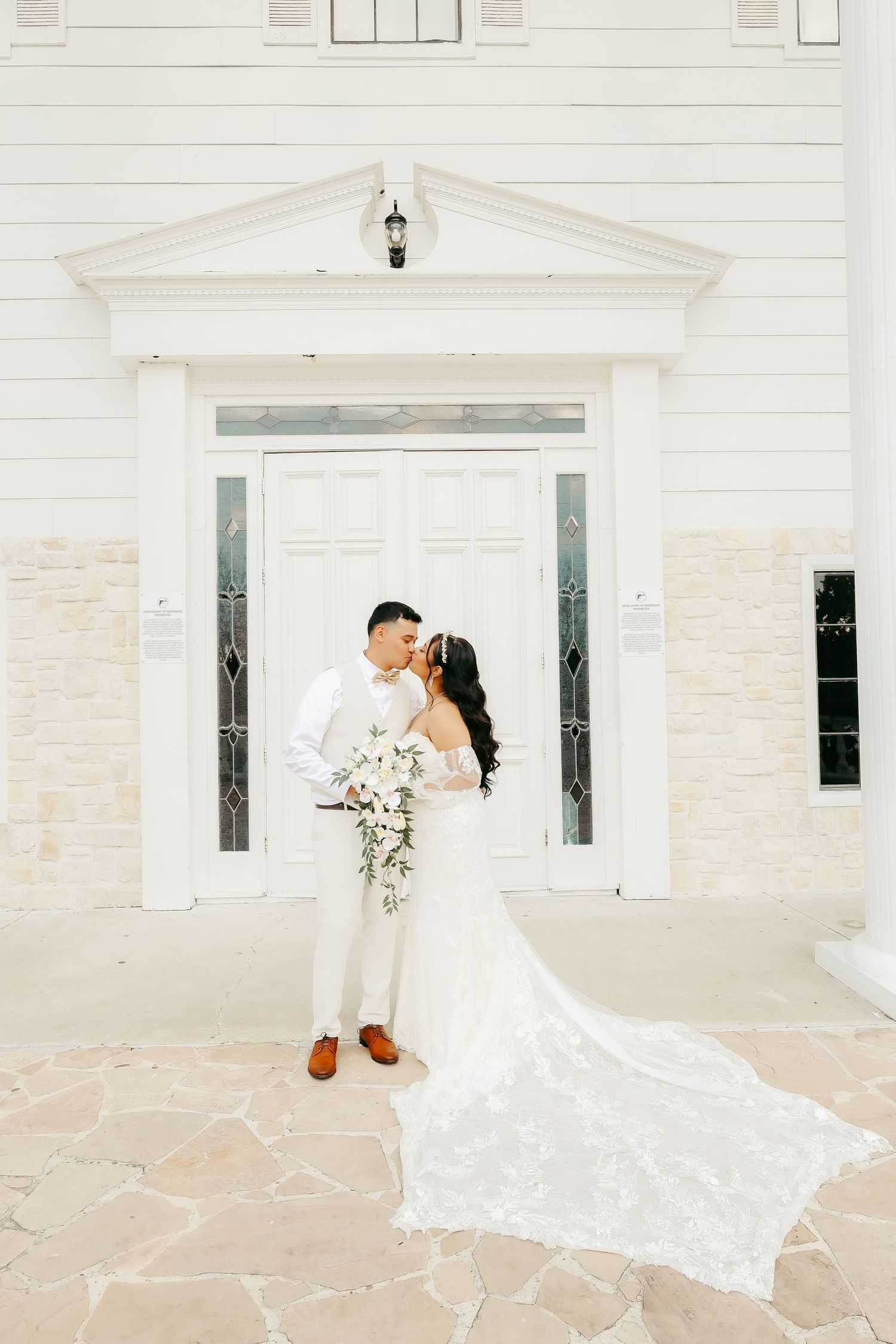 Elegant wedding photo of couple in front of white chapel entrance with detailed architecture.