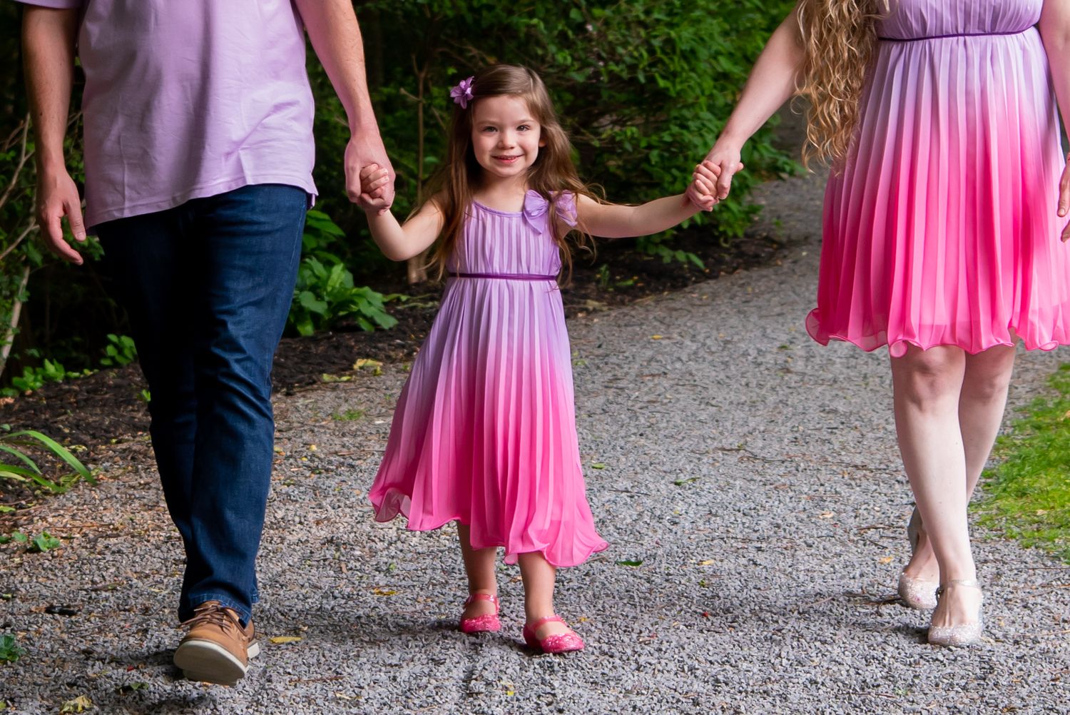 family walking toward camera, focus on four year old girl holding parents hands