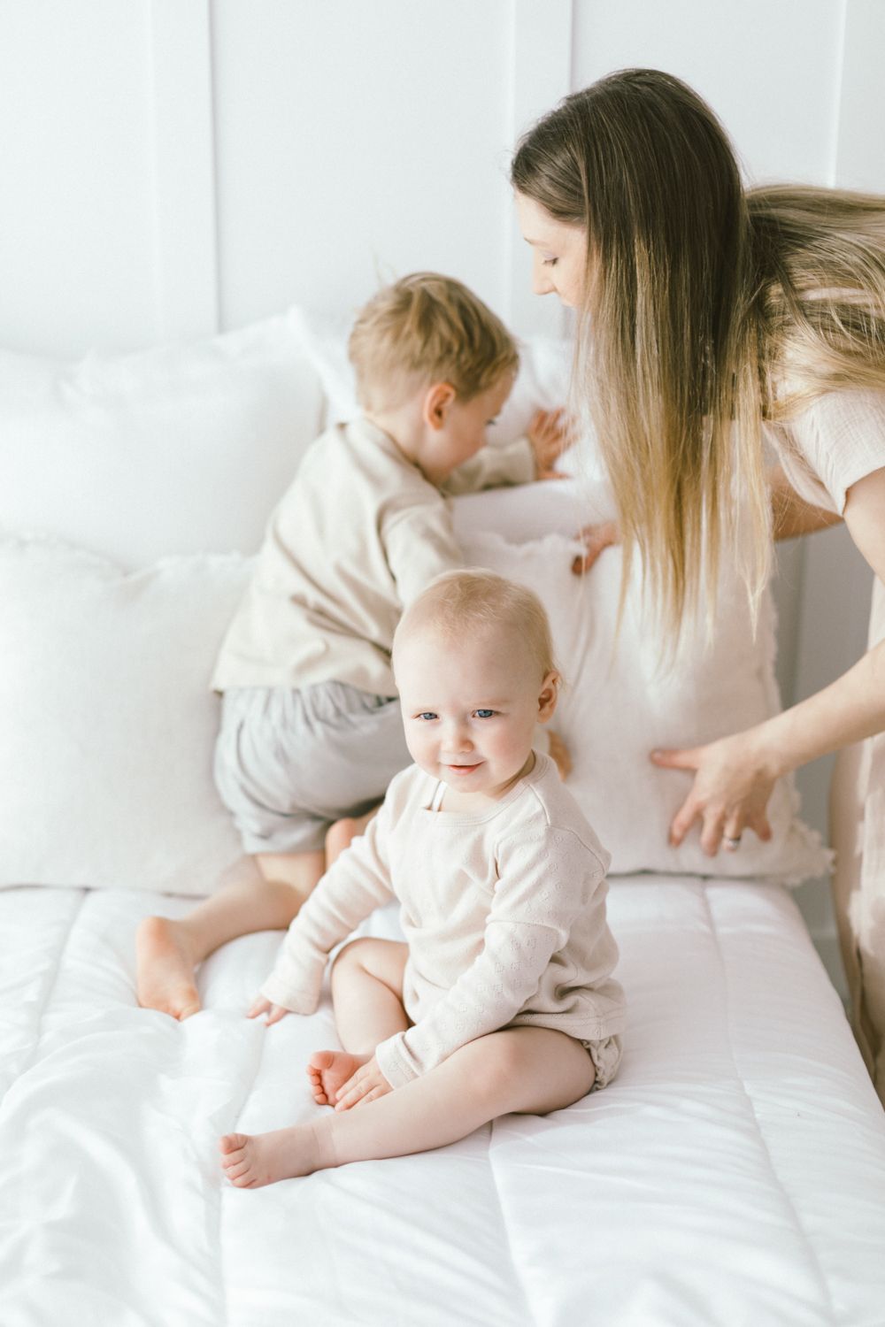 Family sharing playful moments on white bedding in bright room.