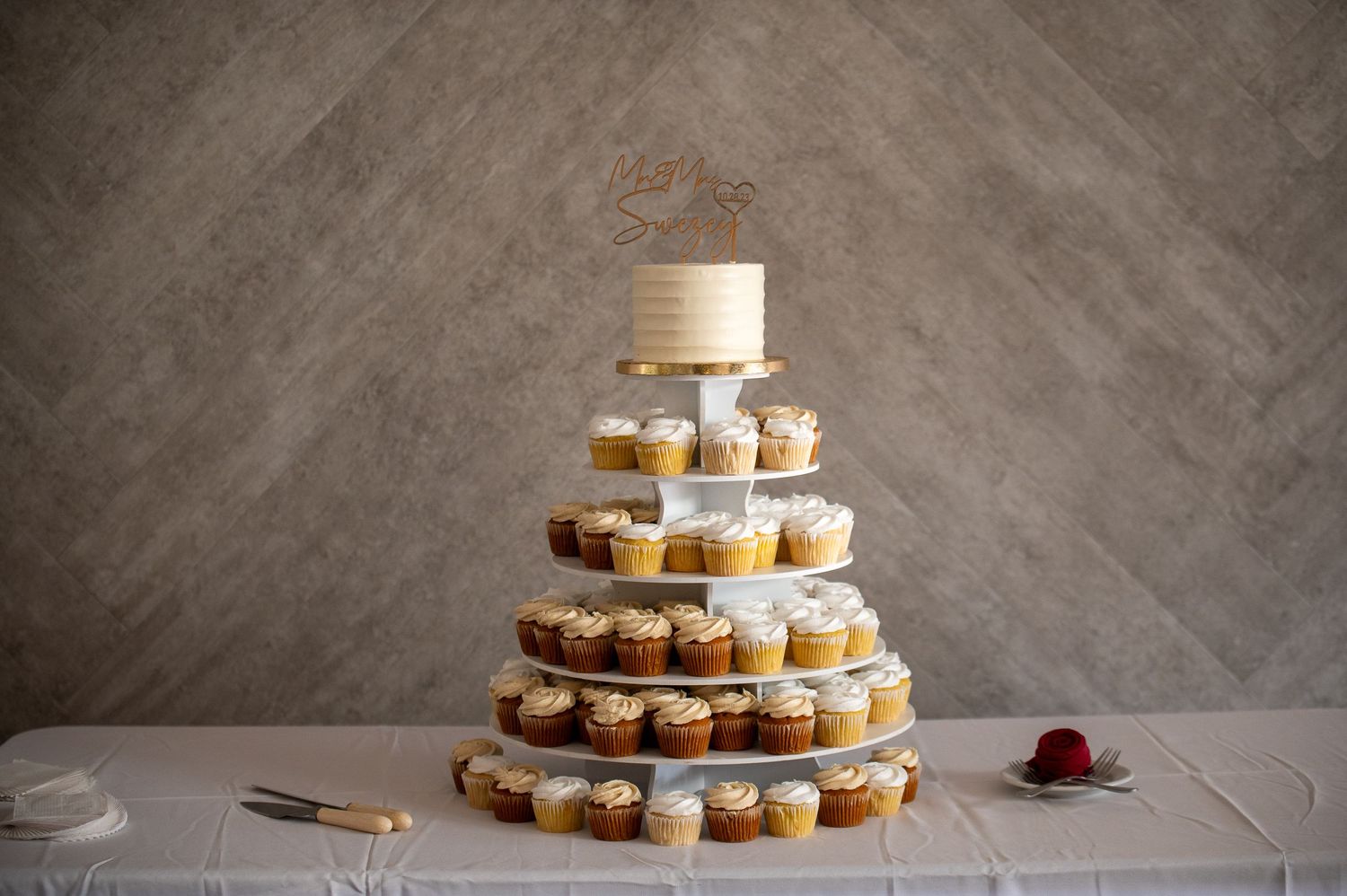 Multi-tiered wedding cupcake display with a small cake topper arranged on white stands.