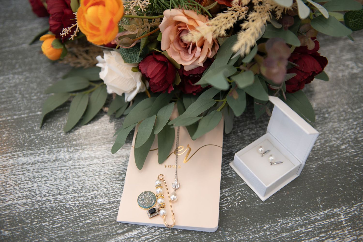 Wedding floral arrangement with roses in orange, pink and burgundy with eucalyptus leaves and jewelry.