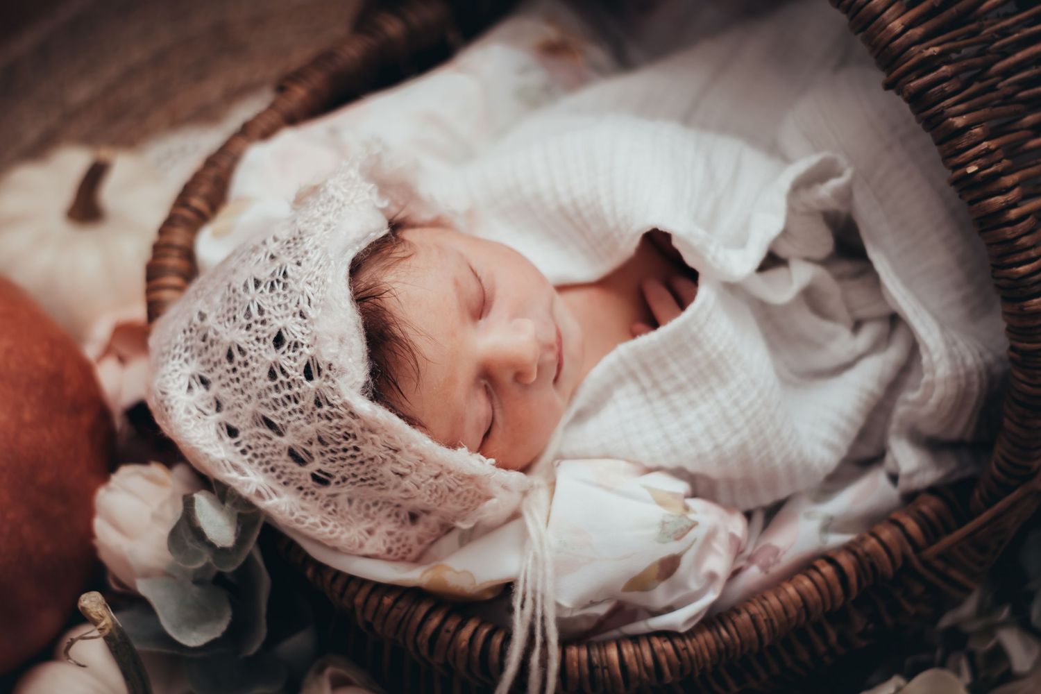 sweet baby girl purses her lips and sleeps wrapped in blankets in a basket for newborn session