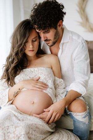 Tender maternity moment captured on a textured pouf with rustic decor elements.