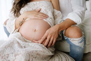 Close up maternity photo showing baby bump with white lace and casual denim styling.