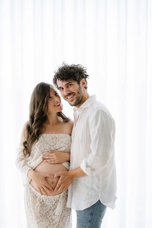Light and airy maternity photo against white curtains showing joyful expectant moment.