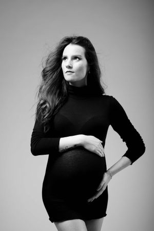 Artistic maternity portrait in black dress showing side profile against neutral background.