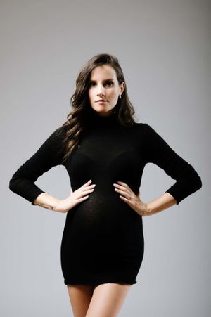 Maternity fashion photo featuring black turtleneck mini dress against studio backdrop.