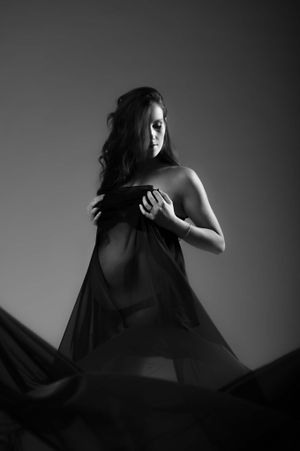 Artistic black and white photo of a woman in flowing fabric creating dramatic silhouette against dark background.