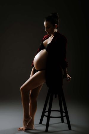 Low-key artistic maternity portrait showing pregnant figure seated on wooden stool.