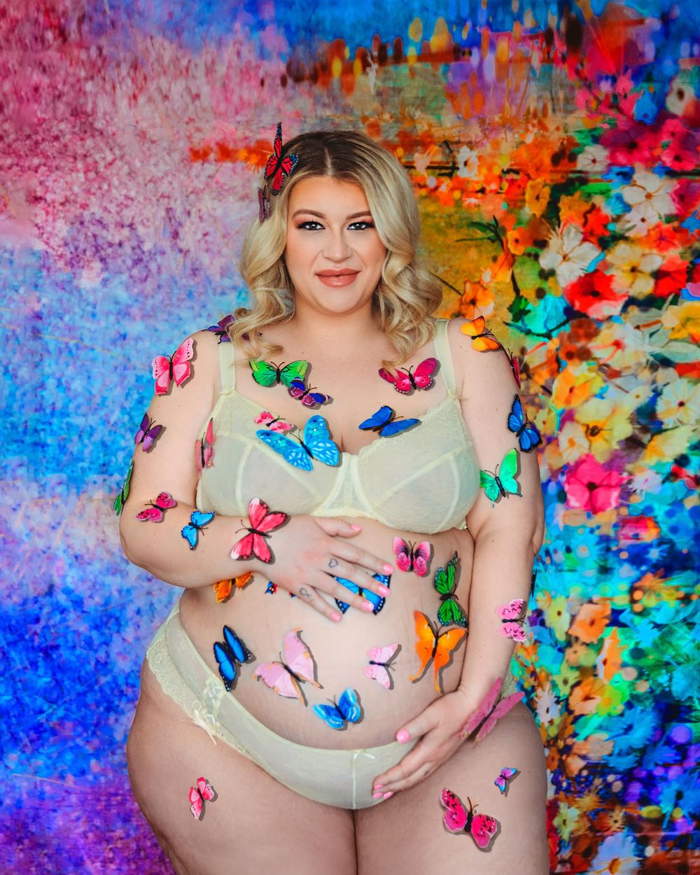 Maternity photo against colorful abstract background with decorative butterflies in sheer beige bodysuit.