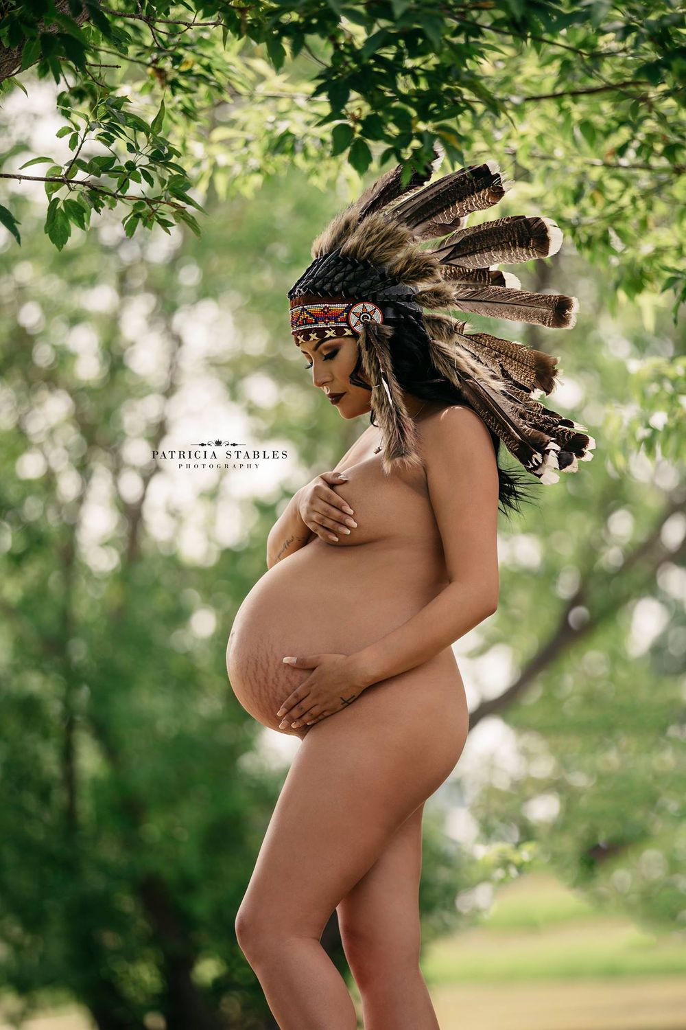 Artistic maternity portrait in nature wearing traditional Native American headdress.