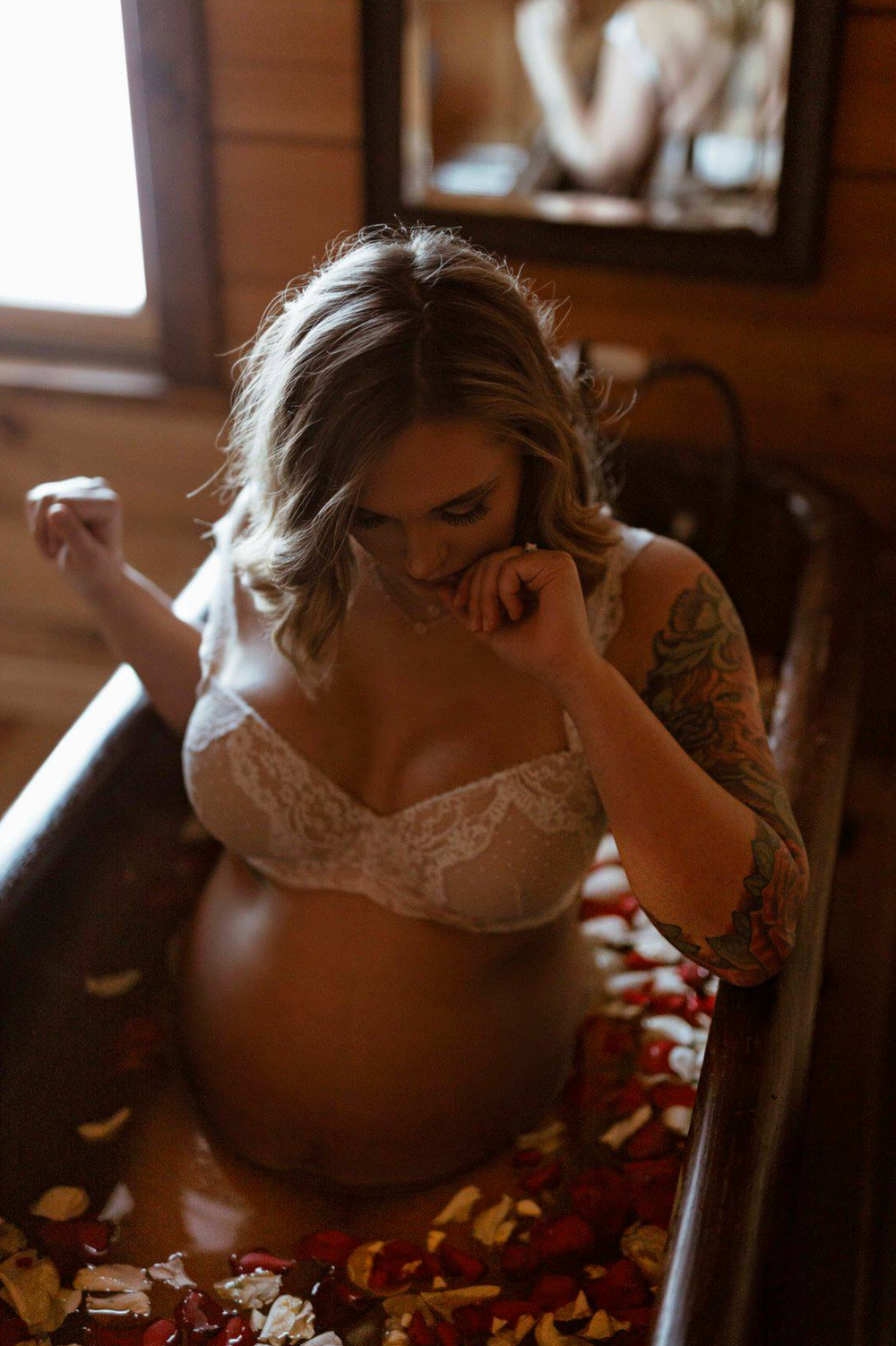 Maternity boudoir photo of pregnant woman in white lace lingerie with rose petals.
