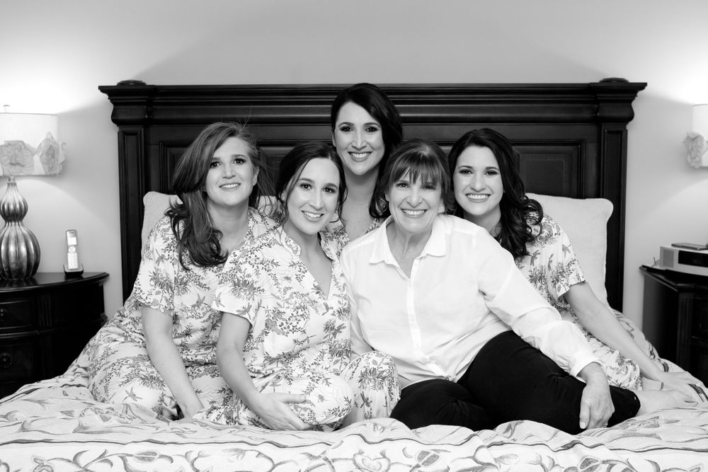 Bridesmaids in floral robes lounging on bed during wedding preparations.