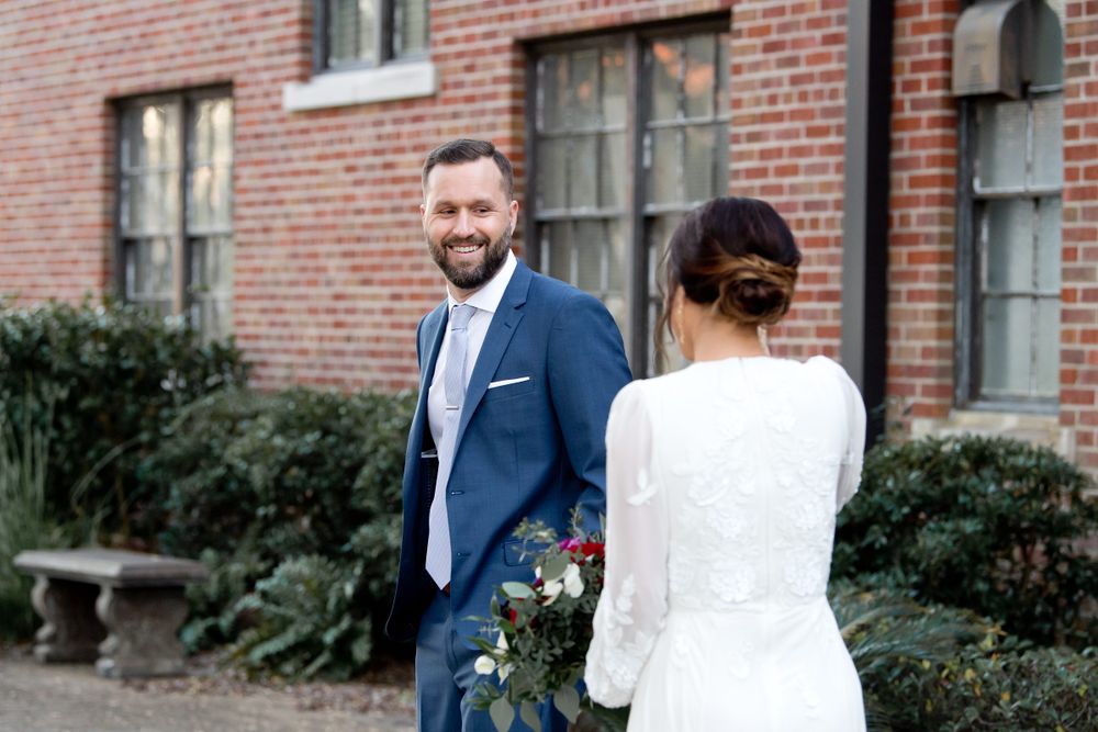 Wedding first look photos against a brick building with greenery.