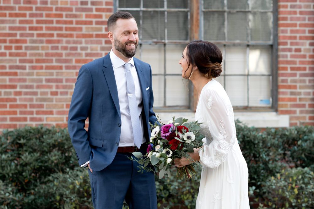 Bride and groom share intimate moments during their first look by a brick building.